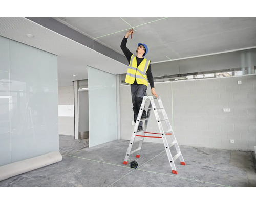 Ein Handwerker steht auf einer Leiter und markiert mit einem Stift Punkte an der Decke, die mit einem Laser ausgerichtet sind.