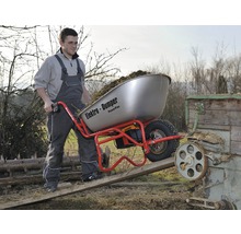 Un homme pousse une brouette électrique chargée avec fonction de basculement sur une rampe