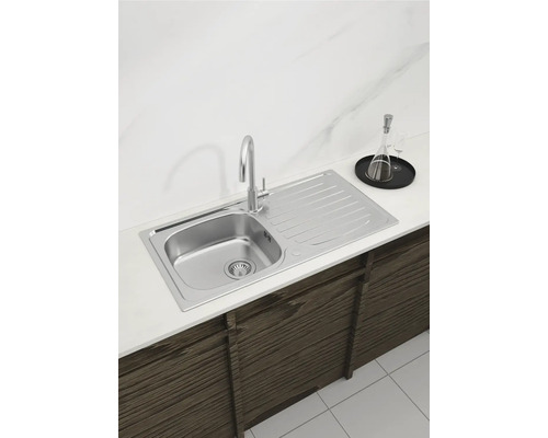 Spüle aus Edelstahl mit Abtropffläche und Wasserhahn in einer Küchenanordnung.