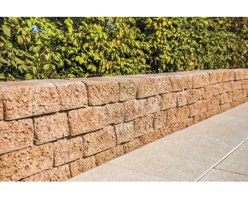 Mauer aus Betonsteinen vor einer grünen Hecke