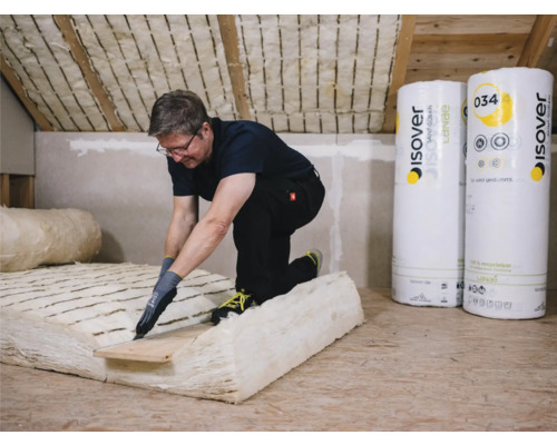 Mann schneidet Dämmmaterial im Dachgeschoss, im Hintergrund sind Rollen von Isover Dämmwolle zu sehen