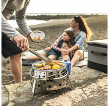 Szene am Strand mit Familie beim Grillen von Garnelen und Zitrone auf einem tragbaren Edelstahlgrill von Petromax