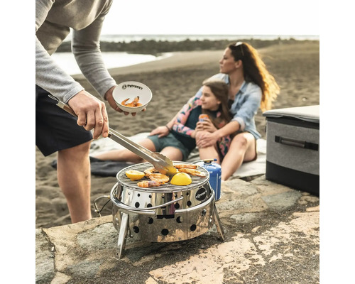 Scène de plage avec une famille faisant griller des crevettes et du citron sur un barbecue portable en acier inoxydable de Petromax
