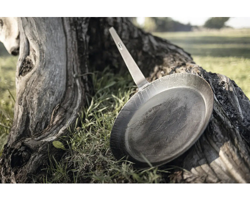 Poêle à frire en métal avec manche posée sur une souche d''arbre à l''extérieur.