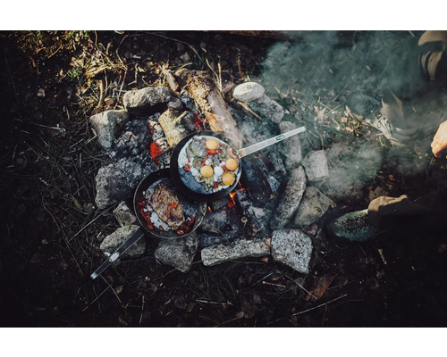 Deux poêles avec des aliments sur un feu de camp, entourées de pierres.