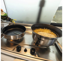 Zwei Töpfe auf einem Herd, in einem Topf kocht Pasta, in den anderen wird Öl gegossen.