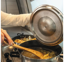 Nudeln werden in einem Topf mit einem Holzlöffel umgerührt, während der Deckel des Topfes angehoben wird.