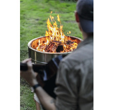 Mann mit Gitarre sitzt vor einer Feuerstelle im Garten