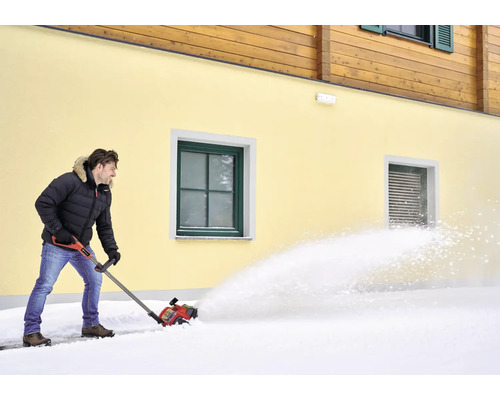 Mann räumt Schnee mit einer Schneefräse vor einem Haus