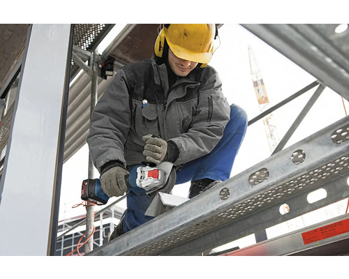 Artisan coupant une pièce à l'aide d'une meuleuse d'angle sans fil sur un échafaudage.