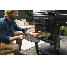 Un homme prépare un barbecue à charbon de bois avec une grille et une pierre à pizza