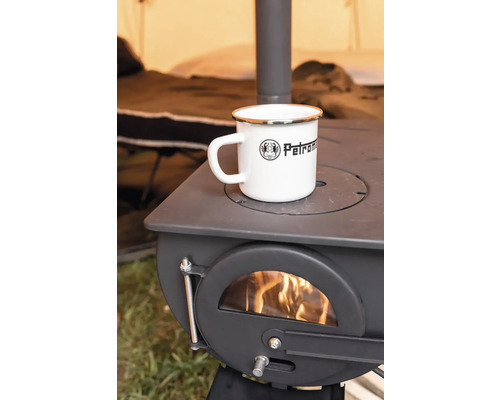 Une tasse en émail Petromax posée sur un poêle à bois Petromax dans lequel brûle un feu.