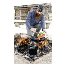 Mann kocht Gemüse in einer Bratpfanne über einem Lagerfeuer im Freien mit einer Kaffeekanne nebenan