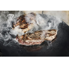 Zwei Steaks mit Rauchentwicklung auf einer Grillplatte