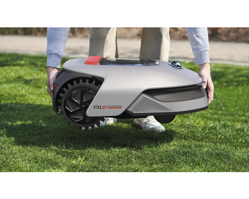 Person trägt einen Rasenroboter über eine Rasenfläche.