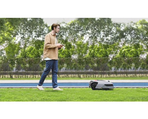 Mann bedient Rasenmähroboter im Garten