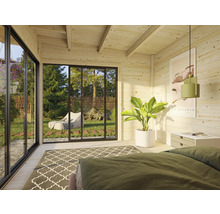 Helles Blockhaus-Interieur mit Bett, Teppich, Pflanze und Blick ins Grüne