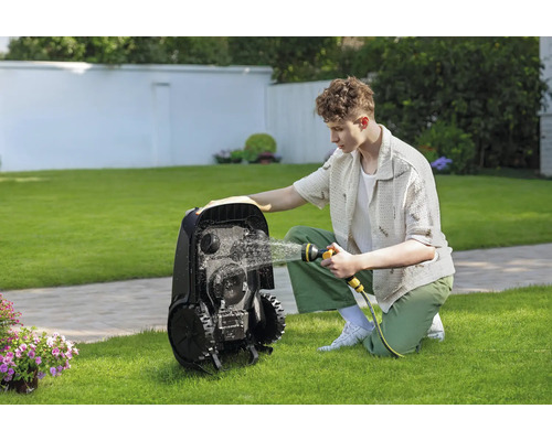 Mann reinigt Rasenmähroboter mit einem Wasserschlauch im Garten