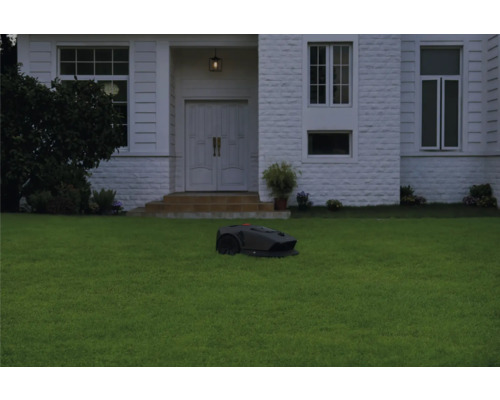 Rasenmähroboter auf Rasenfläche vor einem Haus.