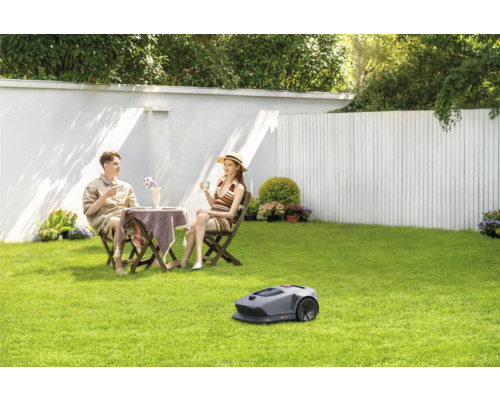 Szene mit Rasenmäherroboter, Paar am Gartentisch auf Rasenfläche