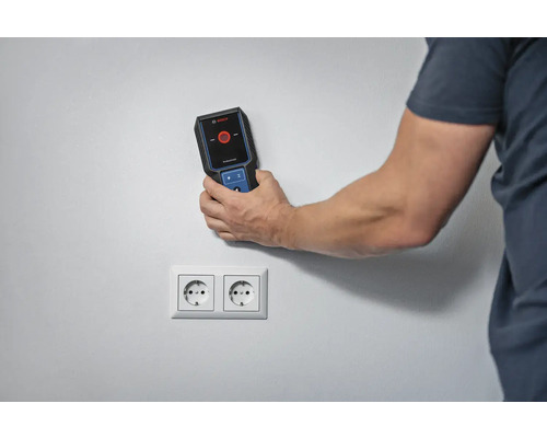 Eine Person verwendet einen Detektor von Bosch Professional, um nach Stromleitungen in der Nähe einer Steckdose zu suchen.