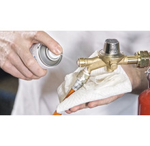 Une personne nettoie un détendeur de gaz avec un spray et un chiffon.