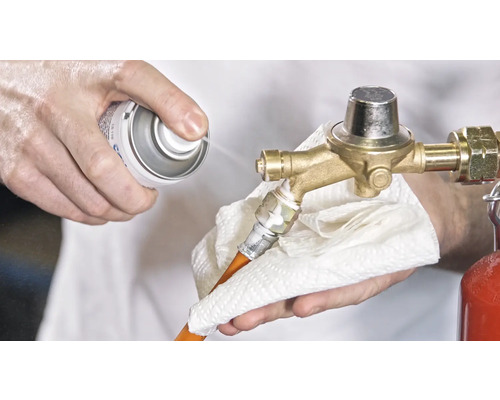 Une personne nettoie un détendeur de gaz avec un spray et un chiffon.
