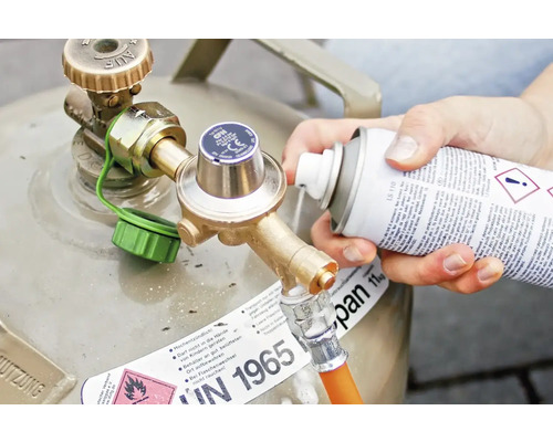 Une personne pulvérise du nettoyant sur le raccord de la bouteille de gaz