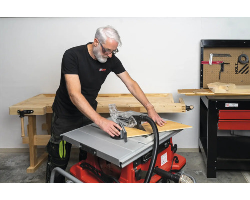 Mann schneidet Holzplatte mit einer Tischkreissäge in einer Werkstatt.