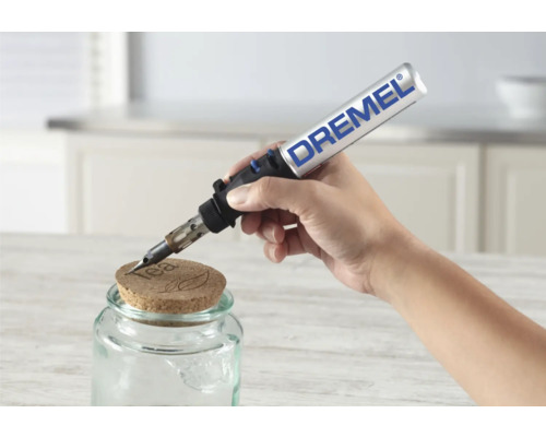 Une main utilise un Dremel VersaFlame pour graver un couvercle en liège sur un pot de confiture.