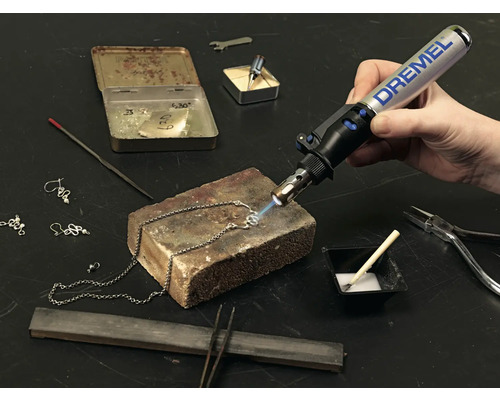 Gros plan d''une personne travaillant sur un collier avec un chalumeau Dremel, ainsi que des outils tels qu''une pince et de la soudure.