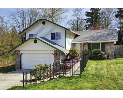 Une maison à deux étages avec garage, clôture et pelouse.
