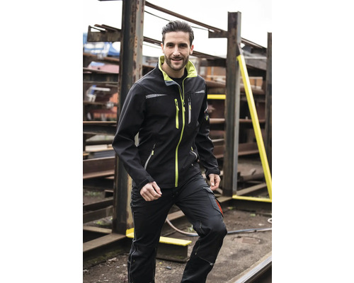 Un homme porte une veste softshell et un pantalon de travail sur le lieu de travail
