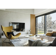 Heller Wohnraum mit Sessel, Couch und Fensterfolie mit Pflanzenmuster.