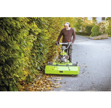 Un homme utilise une balayeuse pour enlever les feuilles mortes sur une route.