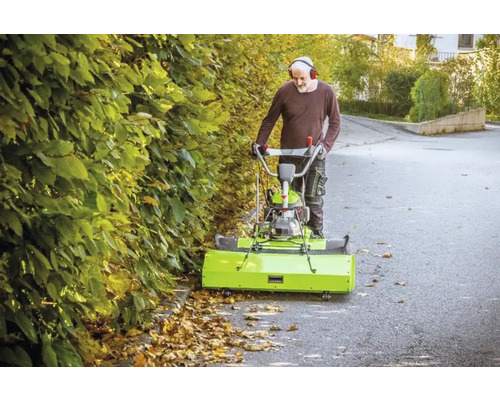Un homme utilise une balayeuse pour enlever les feuilles mortes sur une route.