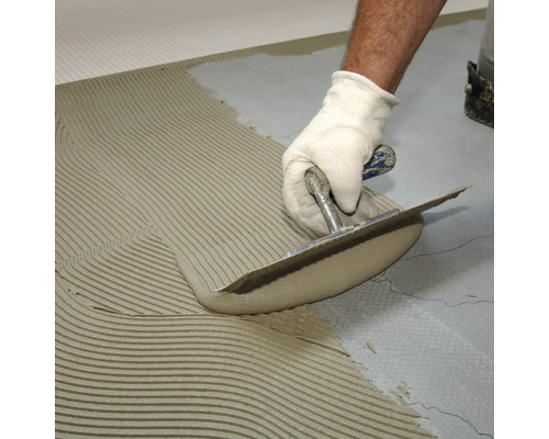 Fliesenleger trägt Fliesenkleber mit einer Kelle auf den Untergrund auf