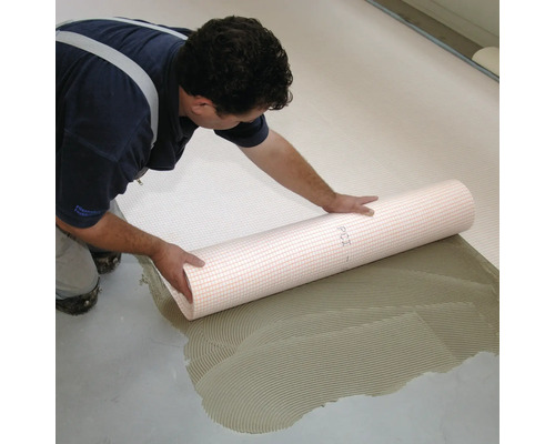 Mann verlegt Entkopplungsmatte auf Estrich mit Fliesenkleber