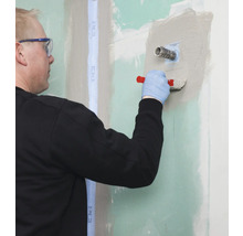 Handwerker spachtelt Wand mit Spachtelmasse und Werkzeug