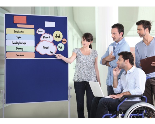 Une femme présente un tableau de présentation bleu avec des notes devant un groupe de collègues.