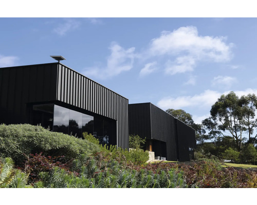 Bâtiment moderne avec des éléments de façade verticaux et de grandes fenêtres en verre, entouré de verdure sous un ciel bleu
