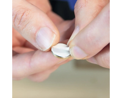 Une personne retire le film protecteur d''un aimant disque.