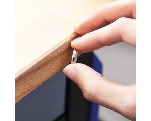 Une personne tient une fine pièce de métal ronde contre un bord en bois.