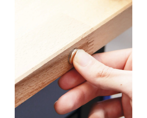 La main fixe la fermeture magnétique sur une planche en bois