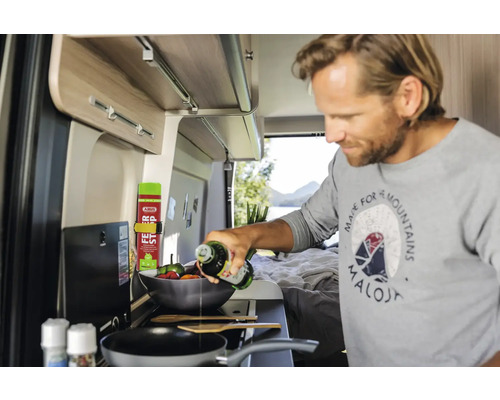 Un homme cuisine dans un camping-car et verse de l''huile dans une poêle.
