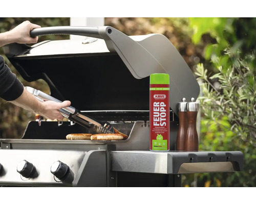 Une personne grille des saucisses avec une pince sur un barbecue, à côté duquel se trouve un spray anti-incendie.