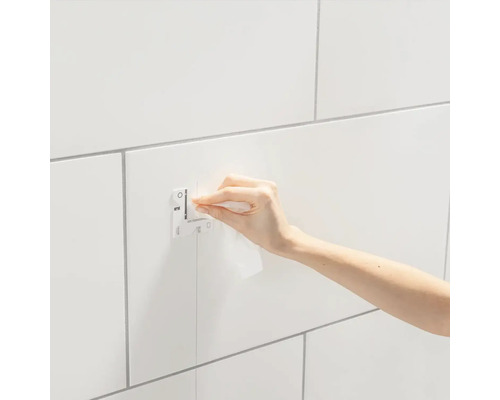 Une personne fixe une plaque de recouvrement Grohe sur des carreaux blancs.