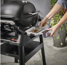 Une femme installe un bac d''égouttement dans un gril Weber.