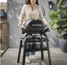Une femme se tient devant un barbecue Weber Q noir sur un support noir.