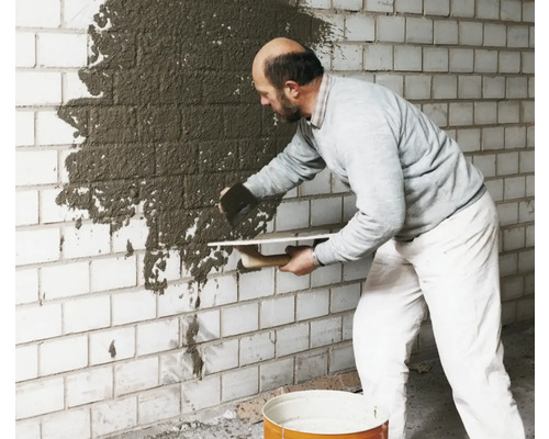 Homme appliquant du plâtre sur un mur de briques